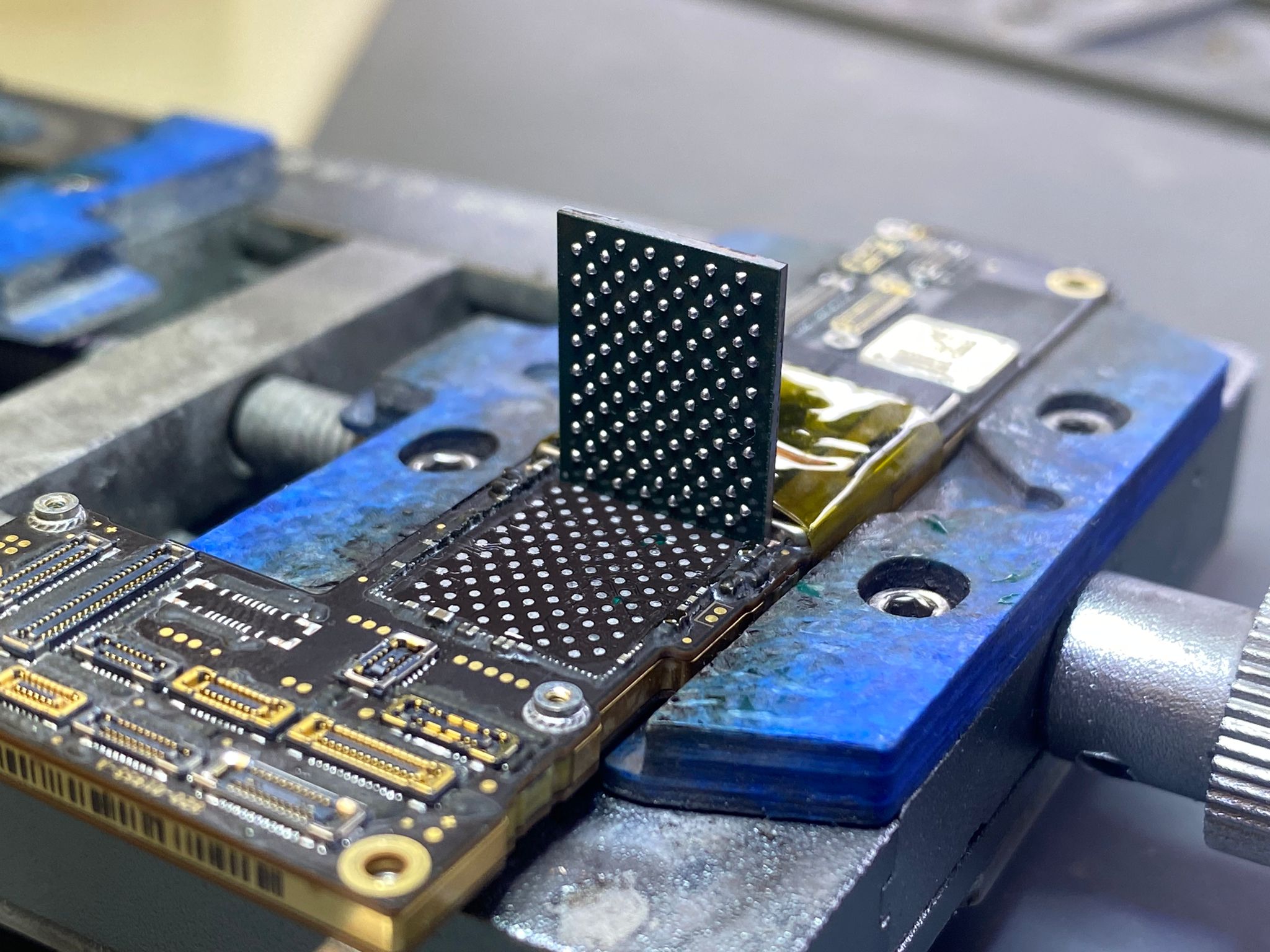 Chip retirado en proceso de reballing sobre placa iPhone en jig azul